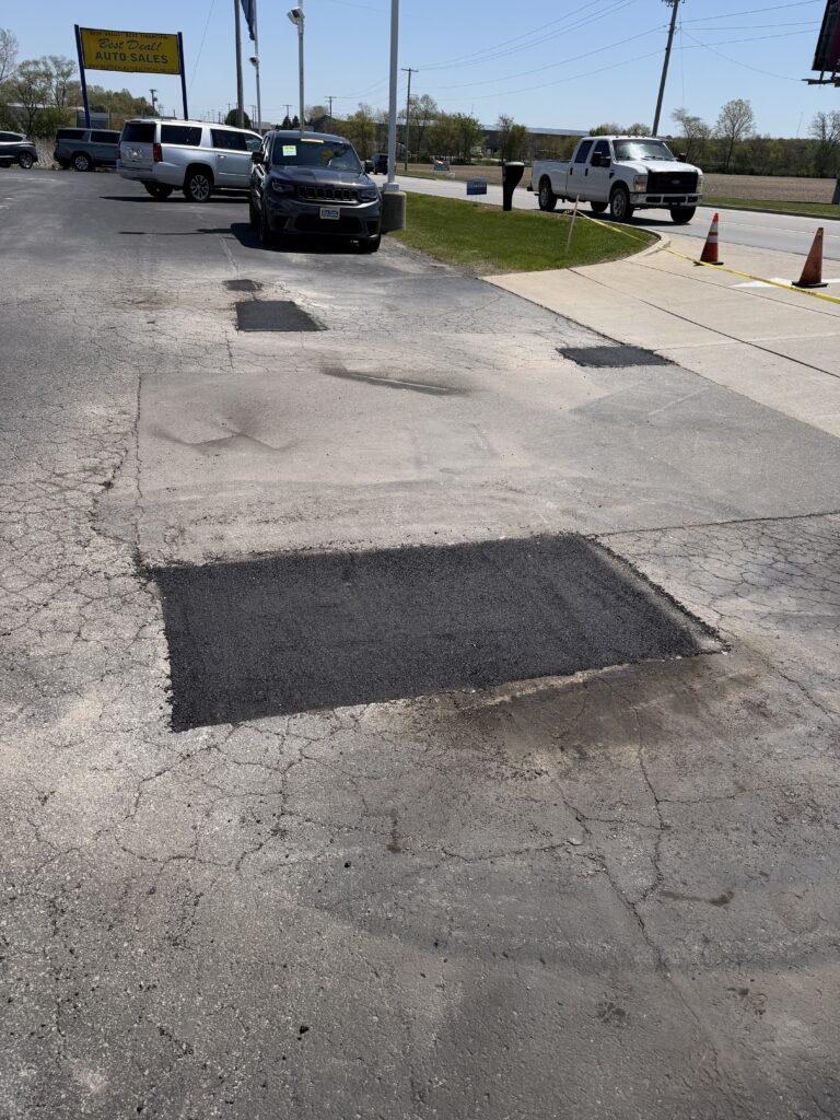 Image of a parking lot that was fixed. You can see a new asphalt patch that was put in.